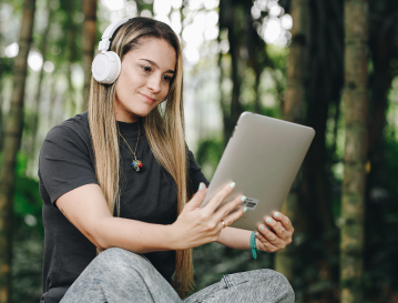 Mujer con audífonos consulta una tableta al aire libre: estudia un diplomado de análisis de datos desde cualquier lugar