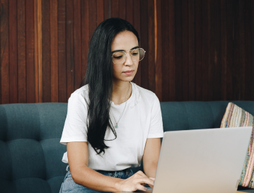 Mujer con gafas concentrada en su portátil sobre un sofá, practicando un dashboard en Excel