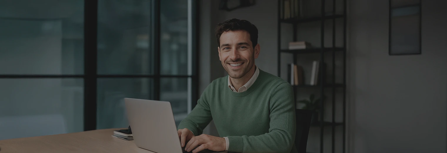 Hombre sonriente con suéter verde frente a su portátil, estudiante del diplomado en gestión pública de EAFIT Virtual