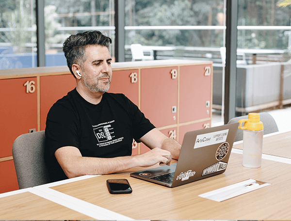 Hombre trabajando en su laptop con un celular sobre la mesa, práctica de posicionamiento con SEO y SEM