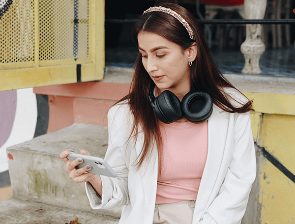 Mujer con audífonos al cuello mira su celular, perfil de analista de riesgos LAFT