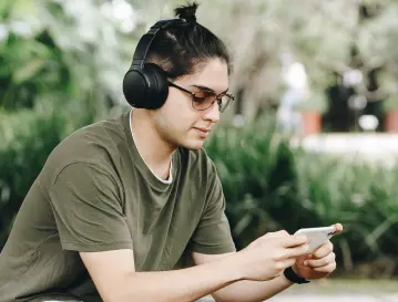 Joven con audífonos y gafas consulta su celular al aire libre, perfil de quien lidera comunidades energéticas