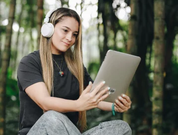 Mujer con audífonos y una tableta en un bosque: diplomado virtual de enfoques ágiles de EAFIT Virtual